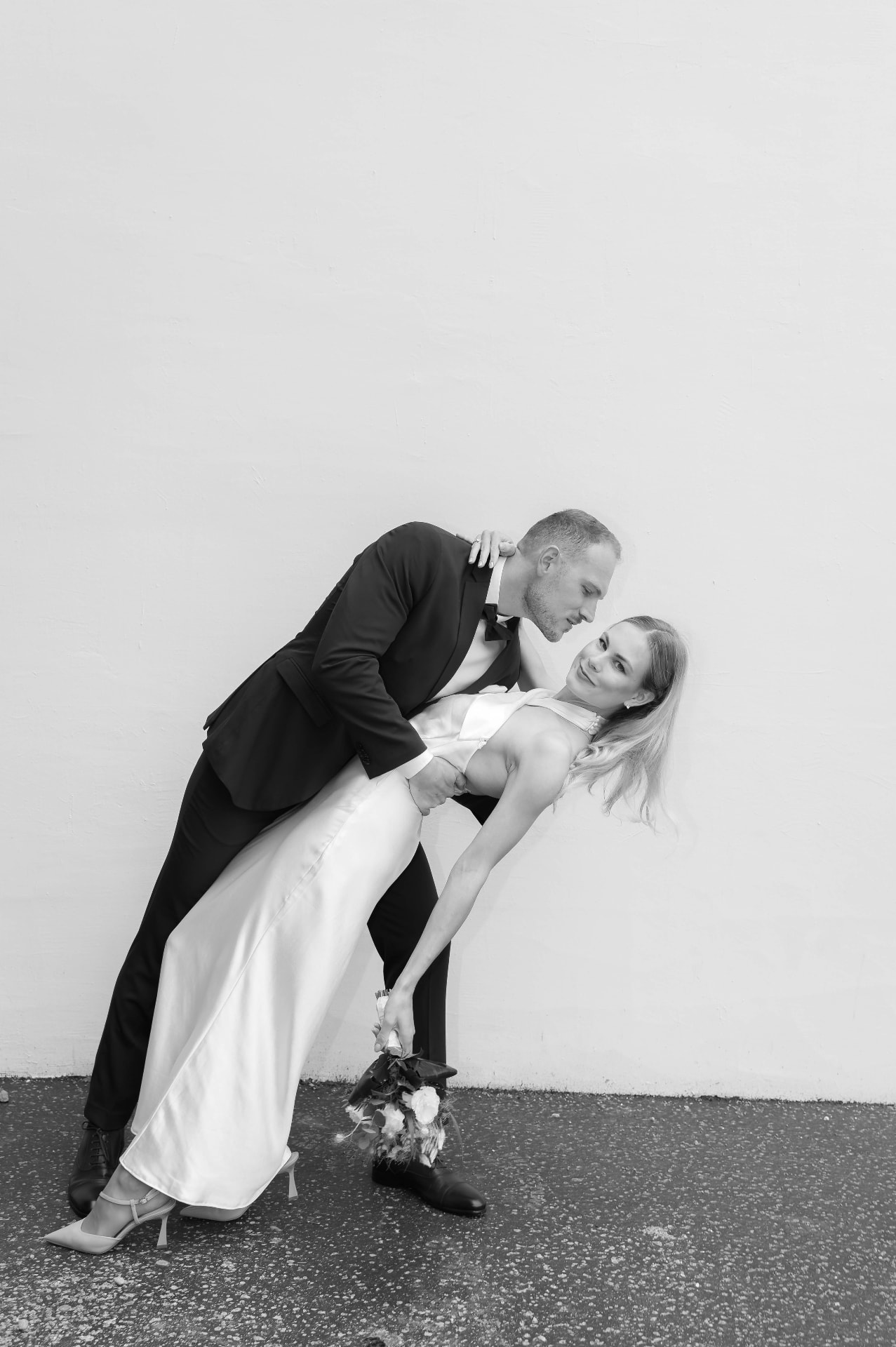Groom dipping the bride in front of a white wall, black and white