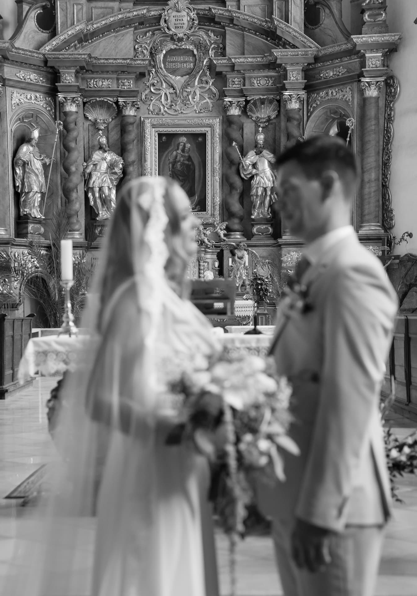 Bride and groom facing each other at the church altar in black and white