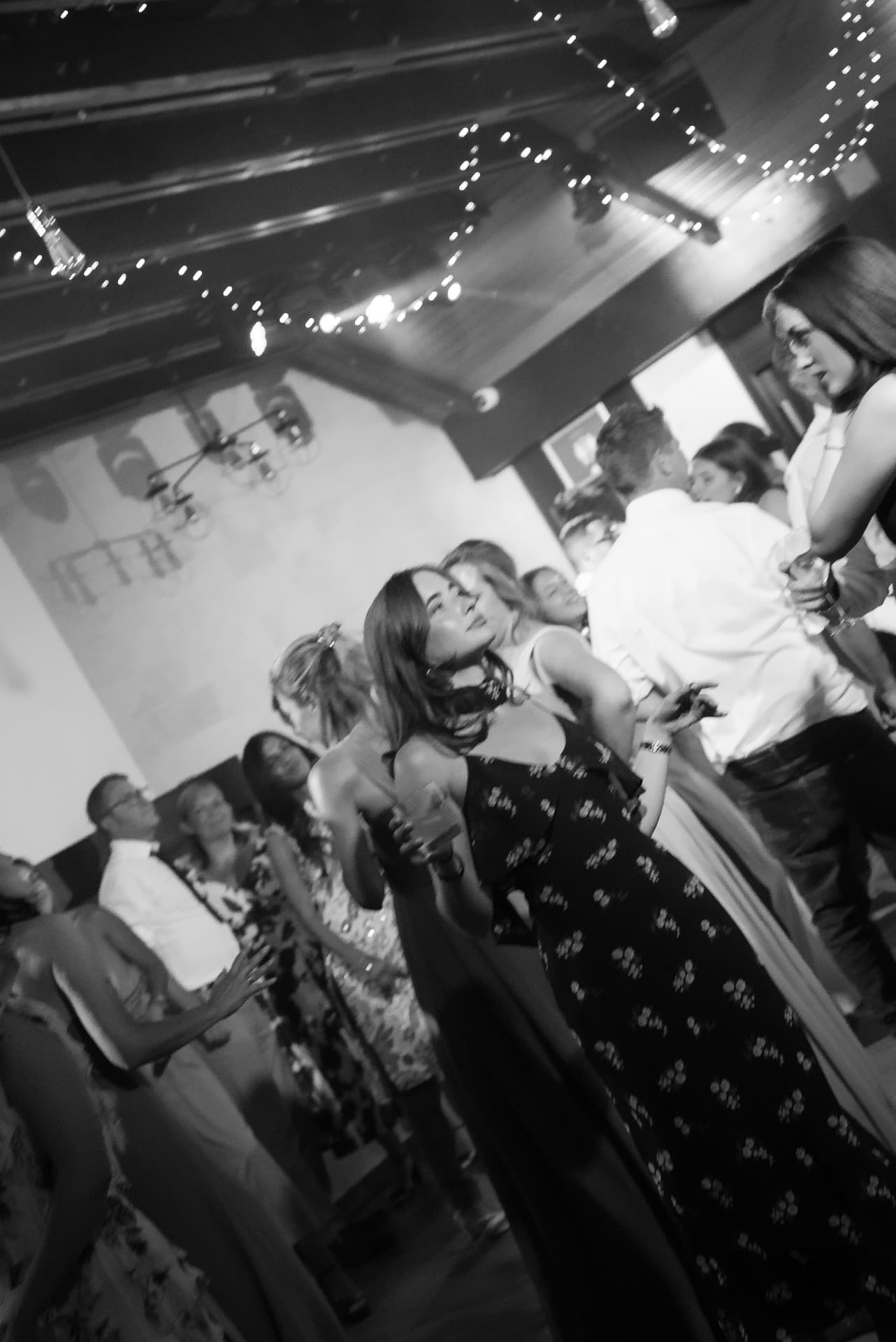 Guests dancing under string lights at the wedding party, black and white