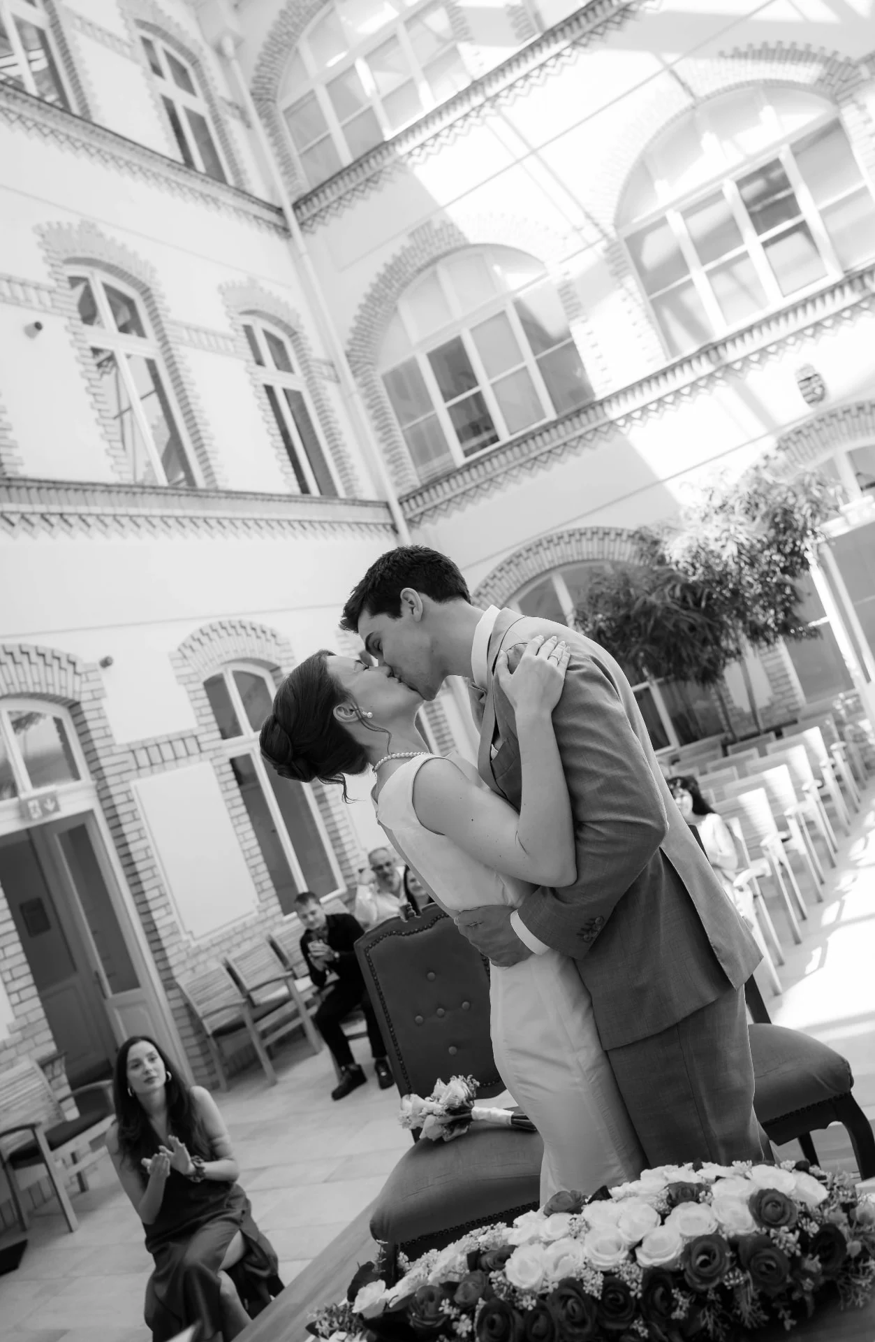 Groom dipping the bride for a kiss in a glass-roofed courtyard, black and white
