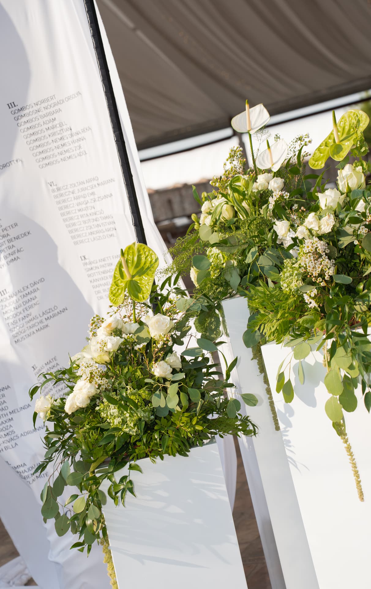 White roses and lush greenery arranged along a modern white wedding seating chart