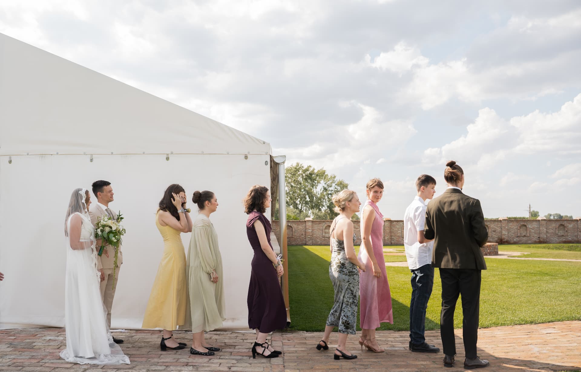 Wedding guests lined up beside a white marquee under a cloudy sky