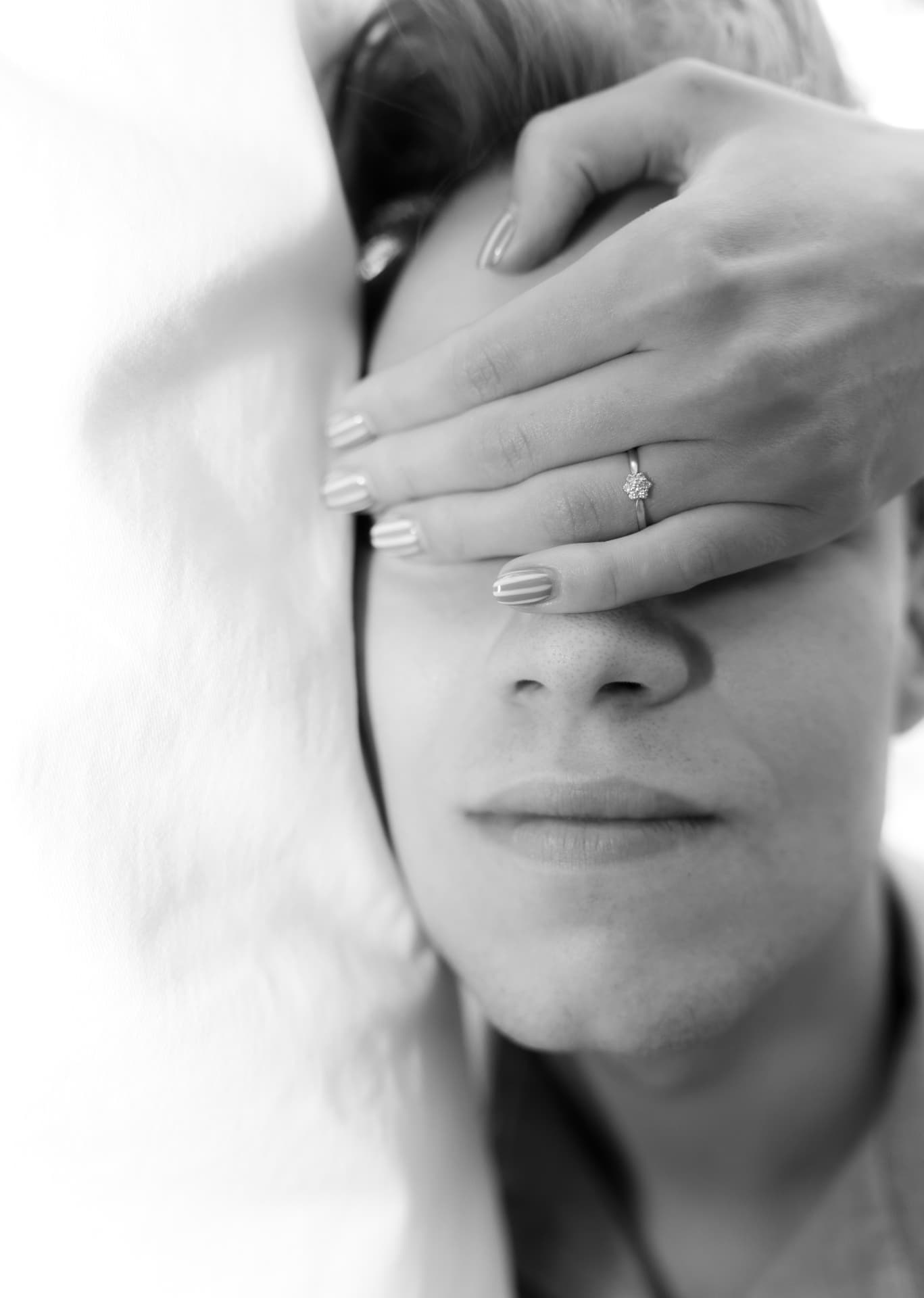 Black and white close-up: hand with an engagement ring covering a partner's eyes