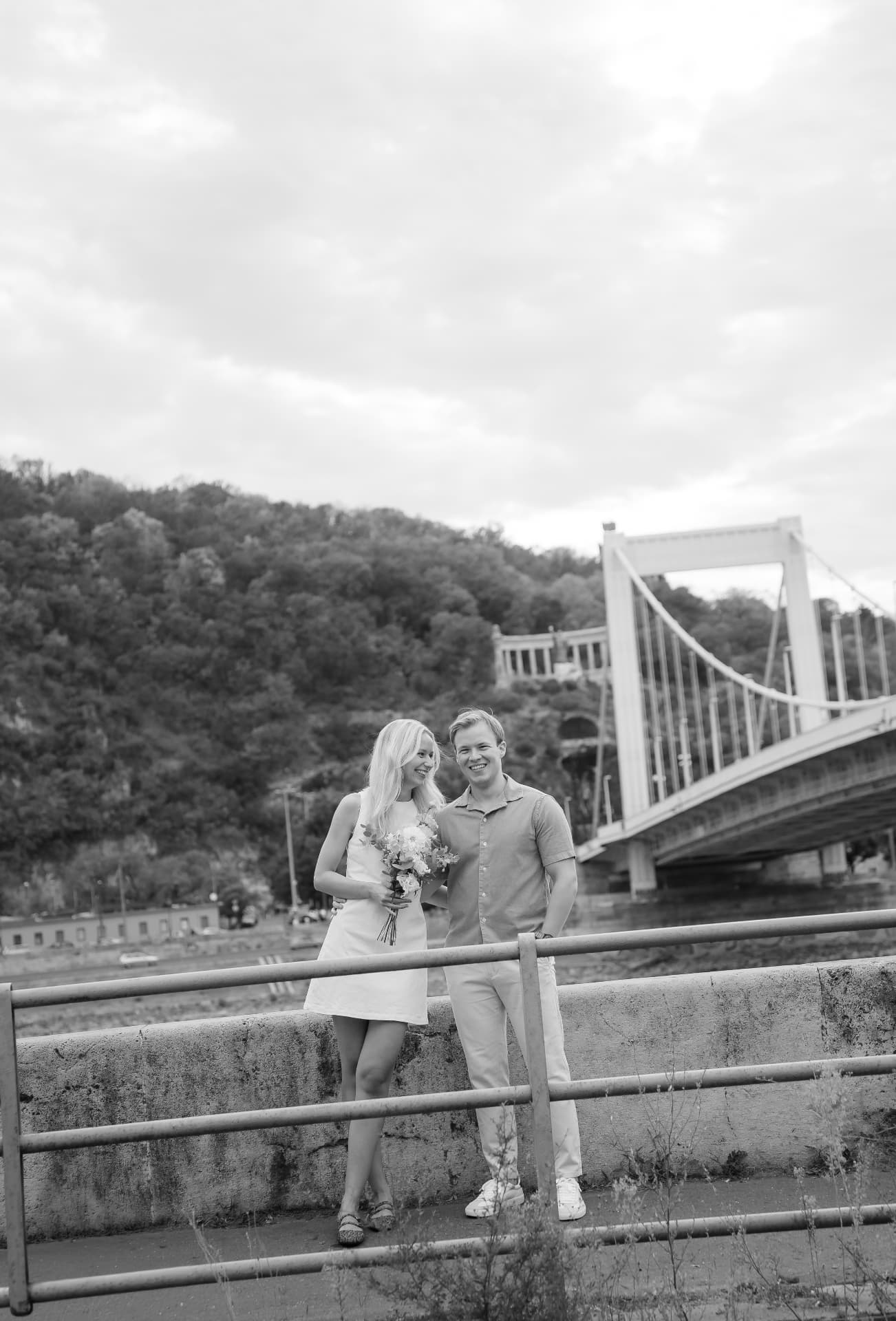 Black and white portrait of a couple by the Danube with the Elisabeth Bridge behind them