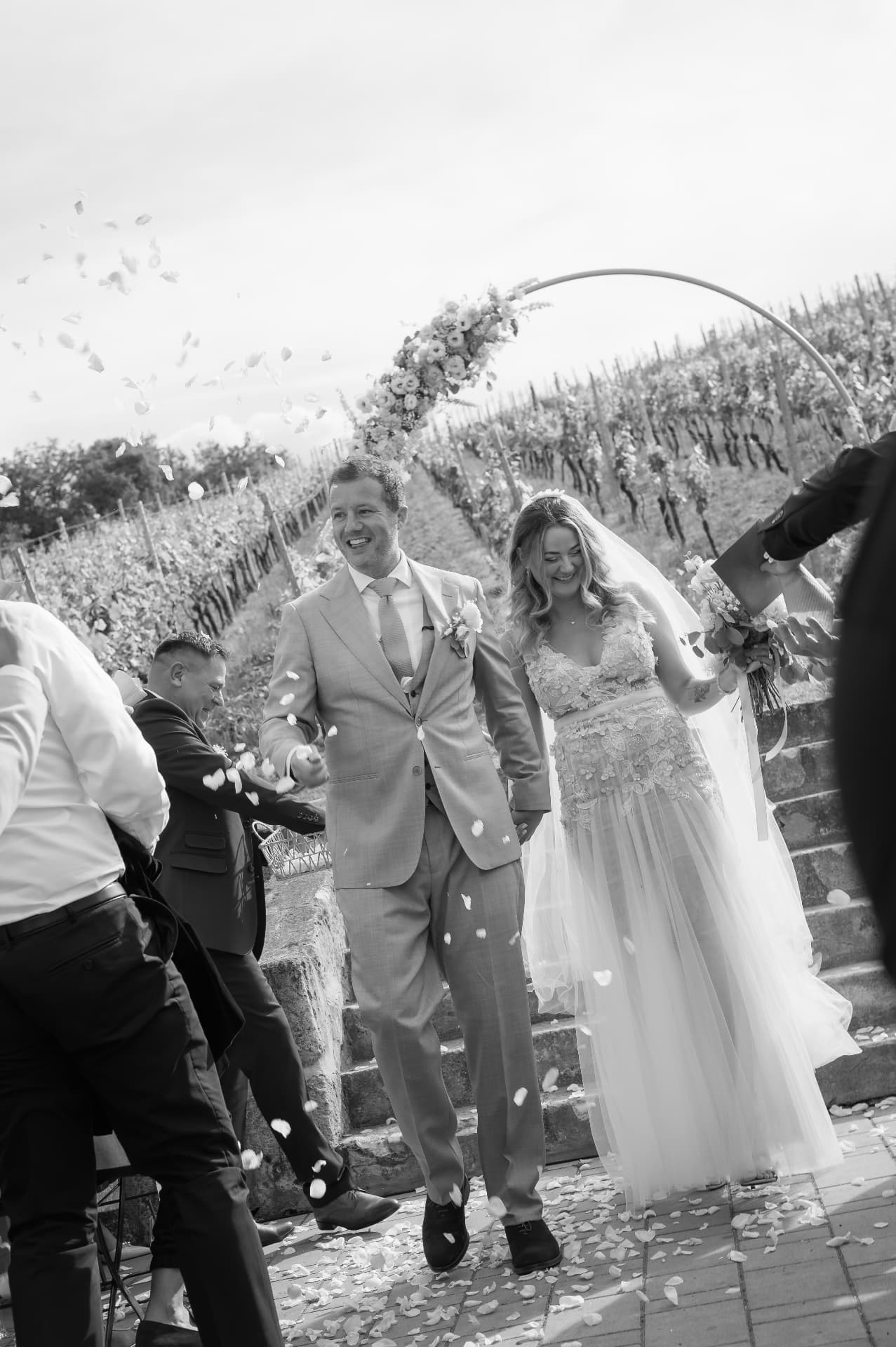 Newlyweds walking down vineyard steps through a shower of petals, black and white
